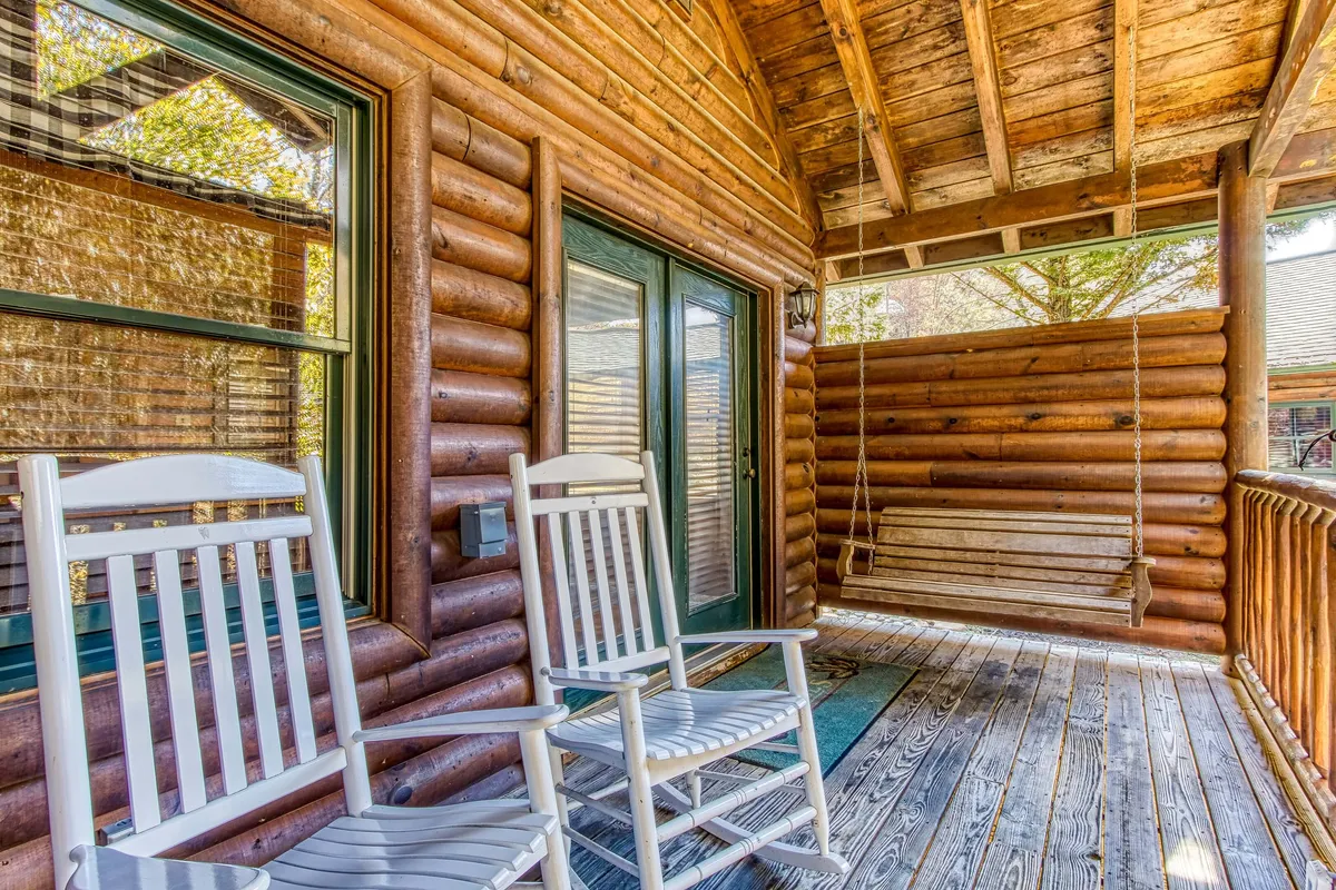 A classic porch scene featuring rocking chairs, a wooden swing, and sturdy log construction, all set amid natural foliage. The setup encourages quiet moments—reading, sipping tea, or simply enjoying the peace of the mountains.