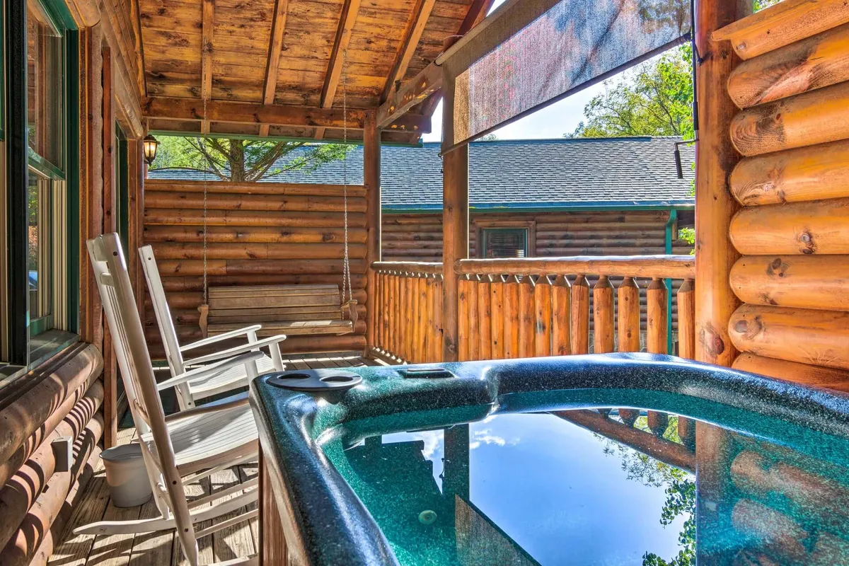 This image showcases a tranquil outdoor hot tub set against the backdrop of wooden cabin architecture and lush greenery. Rocking chairs nearby offer additional spots for couples to relax and enjoy the natural surroundings, while the overall vibe is serene and intimate—perfect for stargazing or sharing a quiet moment.