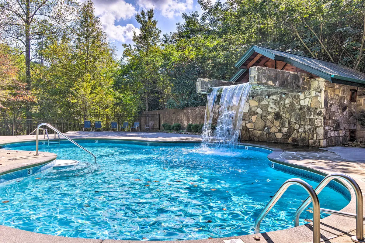 This exterior image captures a sparkling community swimming pool with an elegant waterfall feature, surrounded by stone walls and comfortable lounge chairs. The setting is tranquil and inviting, perfect for both social gatherings and relaxing solo time by the water.