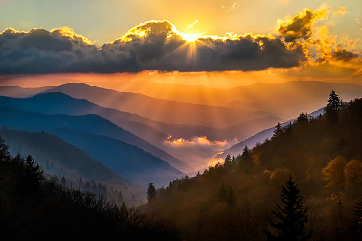 This image captures a breathtaking sunset over mountain ranges with clouds tinged in warm hues, evoking the awe and tranquility of the Smoky Mountains. The scenery invites thoughts of outdoor exploration, romantic hikes, and quiet, memorable moments surrounded by nature’s majesty.