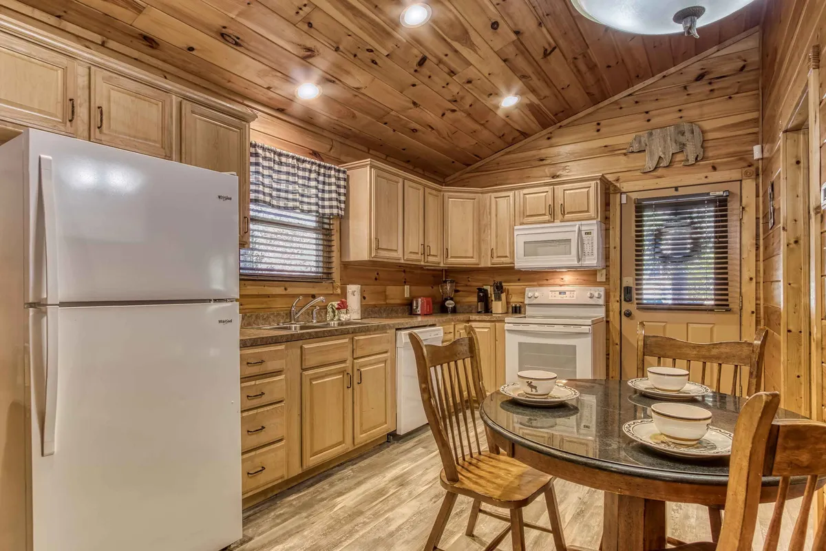 This image features a warm, inviting kitchen with granite countertops, wooden cabinets, a circular dining table, and white appliances. The table is centrally located, suggesting a spot for shared meals and conversation. The space is bathed in natural light, enhancing the cozy ambiance.