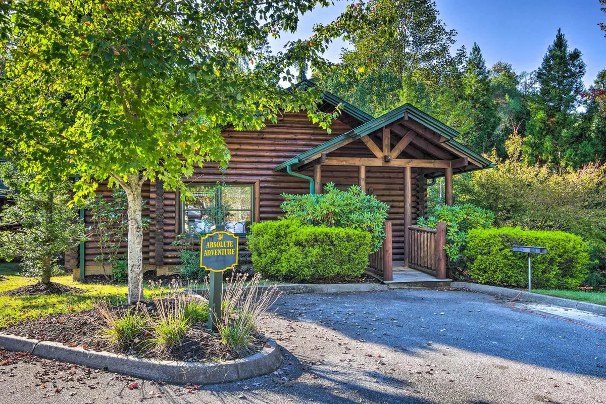 A welcoming view of the log cabin exterior, surrounded by green shrubbery and featuring a visible welcome sign. The porch offers a glimpse of the inviting space where guests can gather before heading out to nearby attractions.